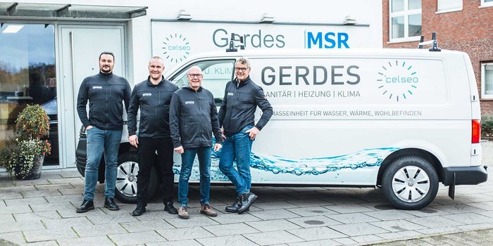 Vier Männer in Arbeitskleidung stehen lächelnd vor einem Firmenfahrzeug mit dem Logo von Gerdes, umgeben von einer modernen Umgebung.