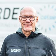 Ein freundliches Lächeln vor einem modernen Hintergrund Ein älterer Mann mit Brille und Glatze lächelt freundlich in die Kamera, während er einen schwarzen Jacke trägt.