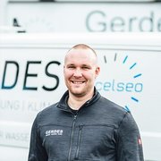Professioneller Handwerker vor einem Firmenfahrzeug Ein lächelnder Mann steht vor einem Lieferwagen mit dem Logo 'Gerdes', der für Dienstleistungen im Bereich Heizung und Klimaanlage wirbt.